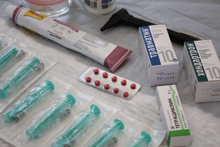 Flat lay of medical supplies including syringes, pharmaceuticals, and an otoscope on a table.